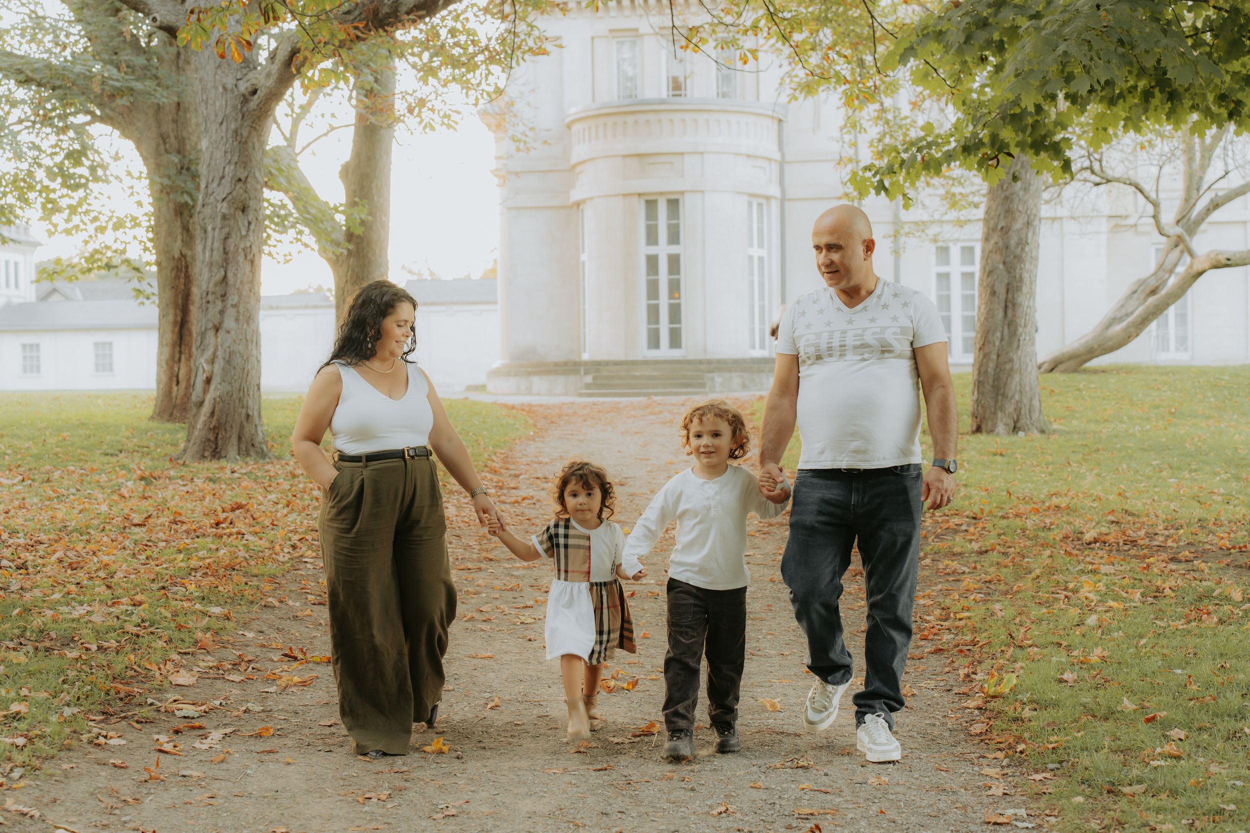 A family of four holding hands on a tree-lined path